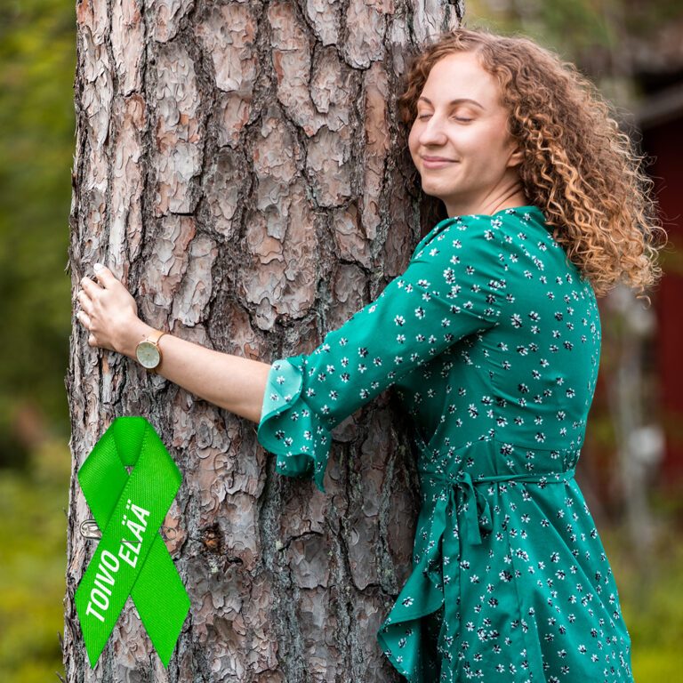 Tyttö halaamassa puuta ja Mieli ry:n mielinauha