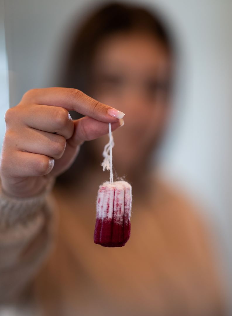 Tyttö pitelee veristä tamponia kädessään.
